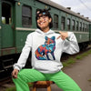 Person in a colorful fox hoodie sitting on a stool near a train.