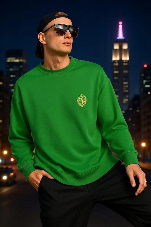Man wearing a green sweatshirt and sunglasses, city skyline in the background.