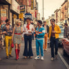 Diverse individuals in retro fashion showcasing 1960s, 70s, and 80s styles on a vibrant urban street