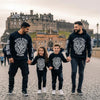 Family wearing Scots Scroll Storm apparel in front of Edinburgh Castle, showcasing Scottish culture and artistic clothing