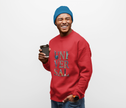 Smiling man in red UNIVERSAL graphic sweatshirt and blue beanie holding coffee