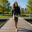 Woman in black sweatshirt and gold patterned leggings walking on a park boardwalk