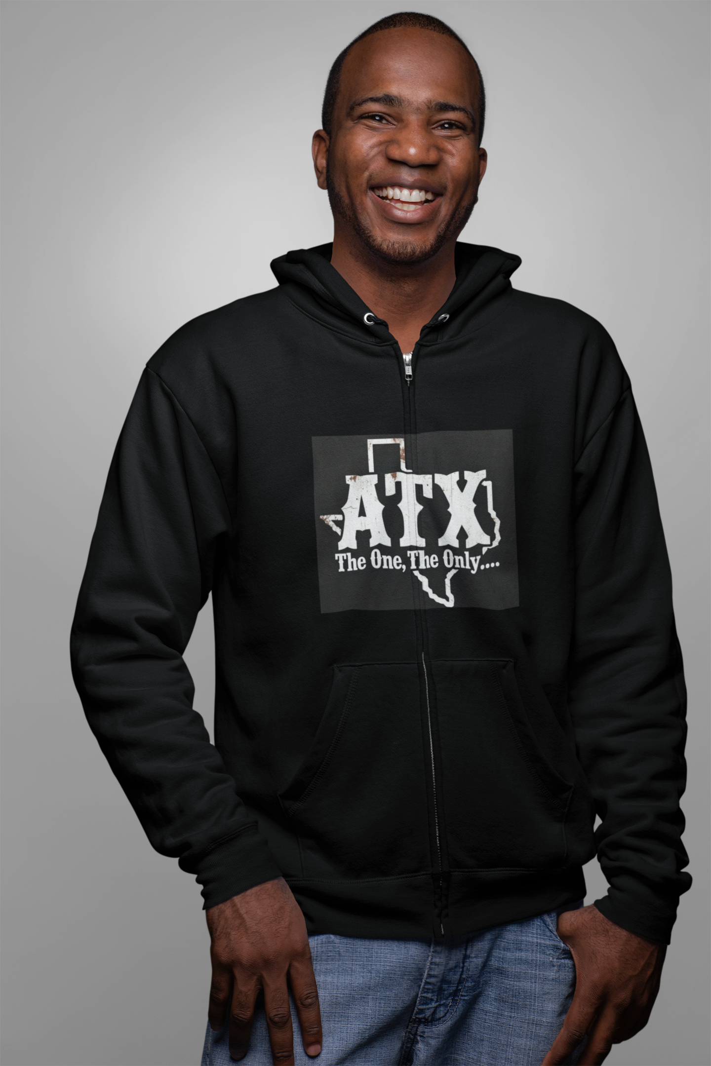 Smiling man wearing a black zip hoodie with ATX Texas graphic and blue jeans