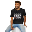 Man in a black graphic t-shirt with race car print and light blue jeans, sitting and smiling