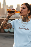 A light blue short-sleeve crewneck t-shirt with the text 'Lipstick Hipster' printed in a dark brown cursive font across the chest, displayed on a solid white background.