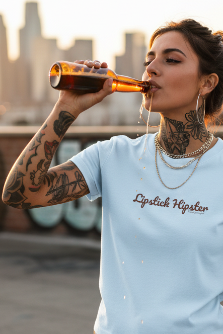 A light blue short-sleeve crewneck t-shirt with the text 'Lipstick Hipster' printed in a dark brown cursive font across the chest, displayed on a solid white background.