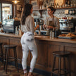 Woman in printed leggings and beige sweater ordering coffee at a cozy café counter.
