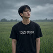 Man in grass looking off into the distance wearing the Touch Grass black t-shirt